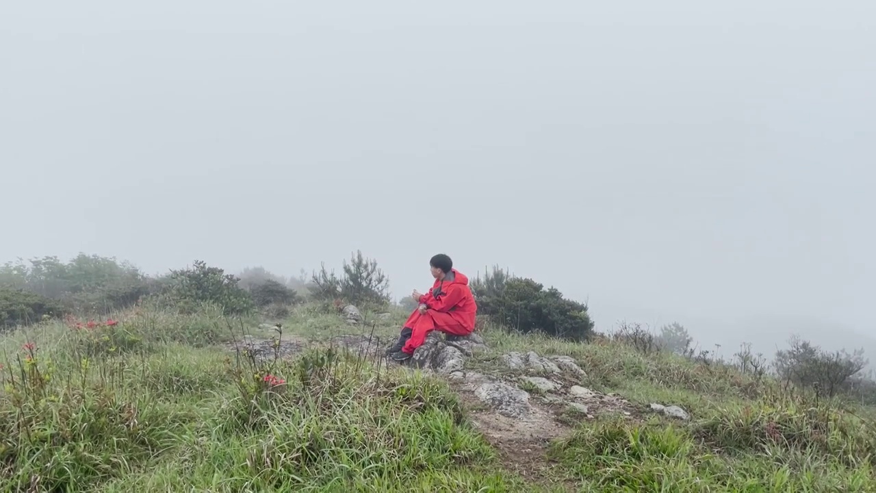 穿红色衣服的显眼登山者坐在大雾中进食视频下载