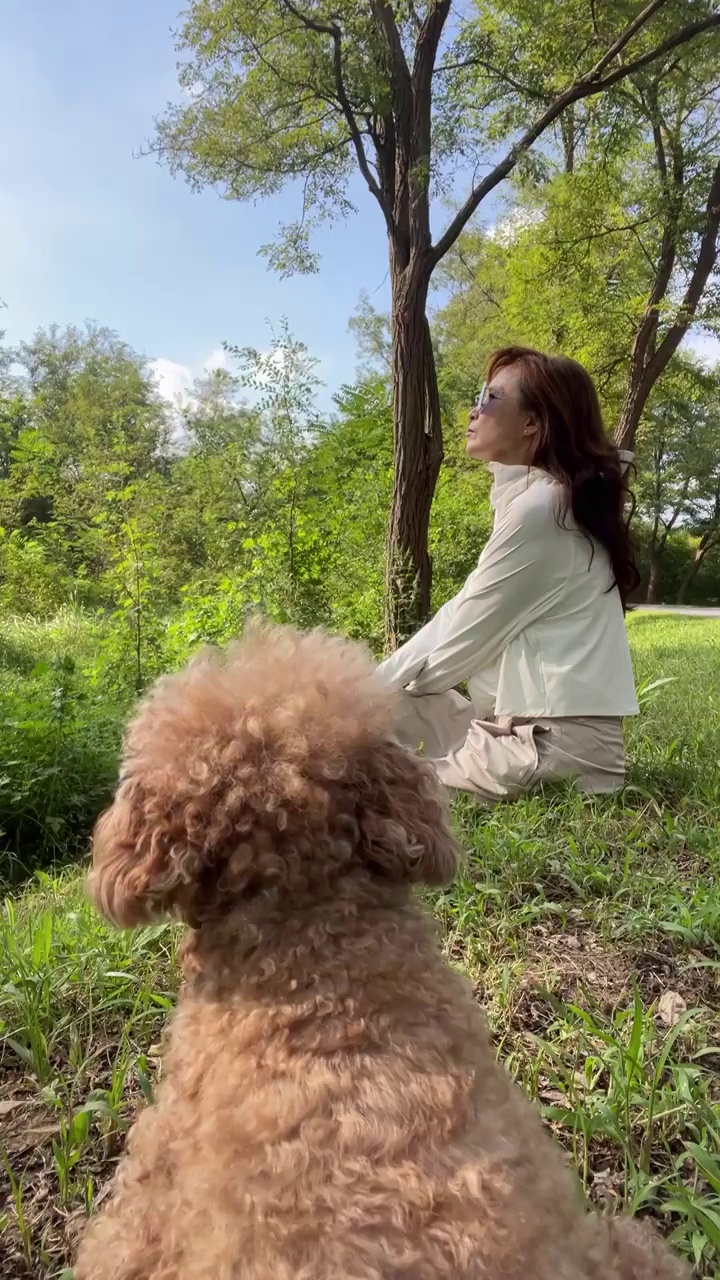 一个点穿防晒服的女人和泰迪犬坐在林间草地上视频素材