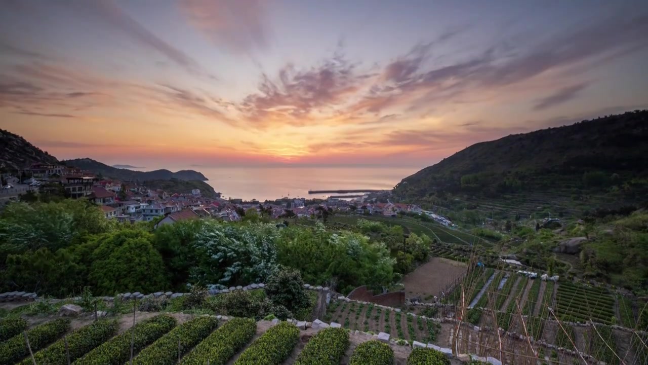 青岛最美青山渔村的日出，夏日的太阳从海湾升起，照亮了美丽的渔村，绿叶红瓦白墙，梦幻的天空视频下载