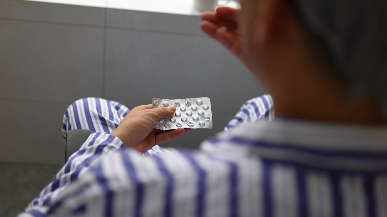 穿着病号服的抑郁症病人坐在窗前吃药的背影视频素材画面3