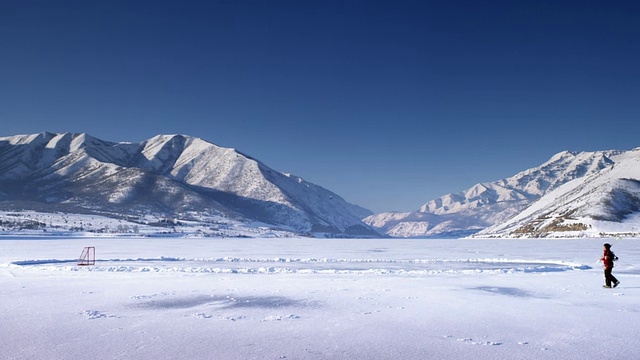 一个遥远的风景镜头，一个被冰雪覆盖的山脉包围的池塘和太阳在顶部闪闪发光。一个人走到球上，然后跨到池塘上。视频素材