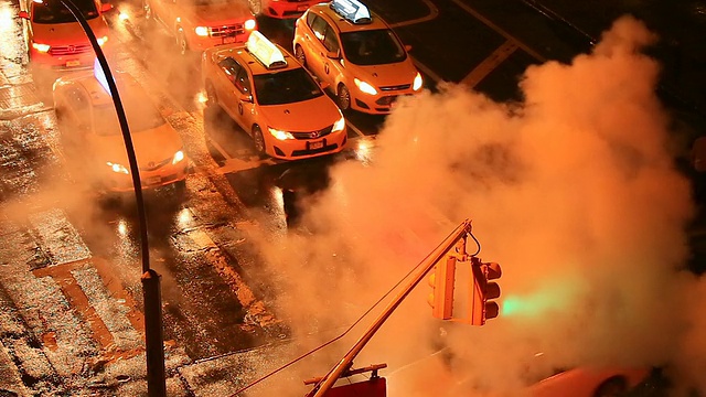 在雨夜，摄像头捕捉到交通信号和周围被从人孔流出的蒸汽包围的交通。视频素材