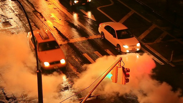 在雨夜，摄像头捕捉到交通信号和周围被从人孔流出的蒸汽包围的交通。视频素材