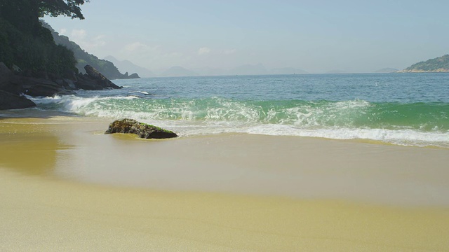 在里约热内卢的红海滩，海浪在沙滩上的一块巨石周围退去和流动的缓慢运动。视频素材