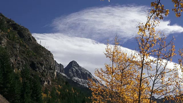 长焦镜头的雪覆盖的山峰与黄色叶树在风中吹拂在前景。视频素材