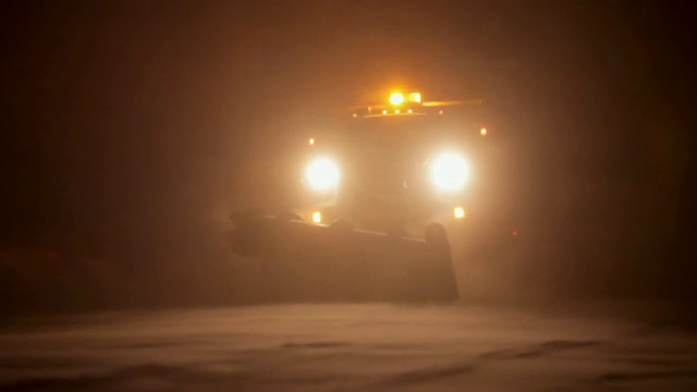 在一个漆黑的夜晚，一辆亮着灯的犁刮着雪视频素材