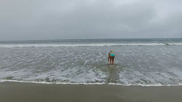 一个迷人的年轻女子穿着比基尼在日出时跑和跳进海里视频素材