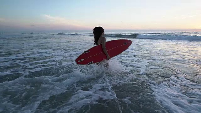 一个年轻女子带着她的冲浪板跑进了水里视频素材