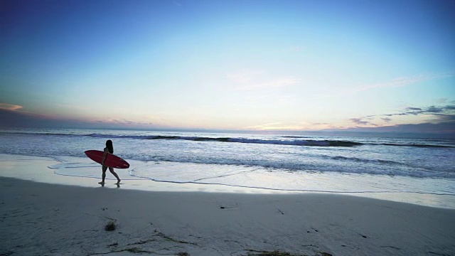 一名年轻女子带着冲浪板在海滩上散步视频素材