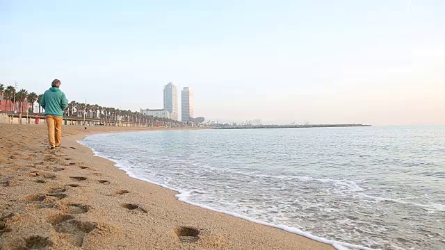 人走在空旷的海滩上，身后是城市建筑视频素材