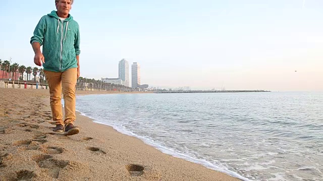 人走在空旷的海滩上，身后是城市建筑视频素材