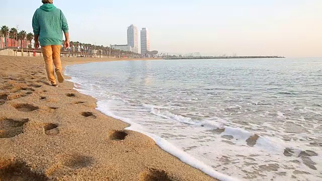 人走在空旷的海滩上，身后是城市建筑视频素材