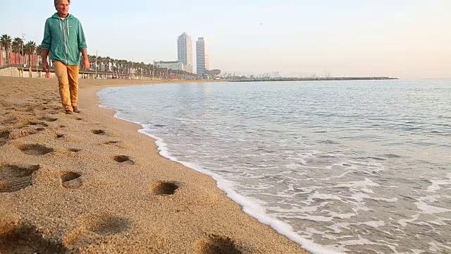 人走在空旷的海滩上，身后是城市建筑视频素材