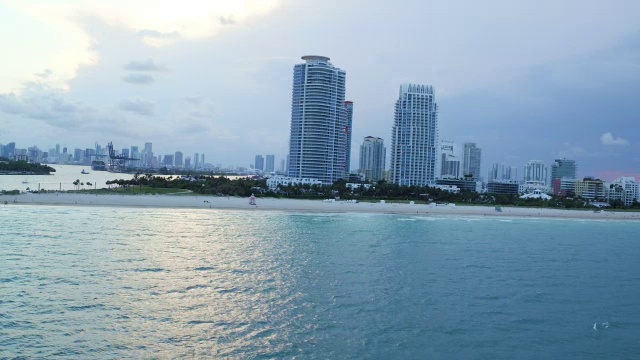 在迈阿密一个阴天的日落，沿着海洋和海滩旅馆进行缓慢的空中扫荡视频素材