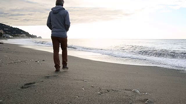 一名男子走在靠近海浪边缘的海滩上，眺望大海视频素材