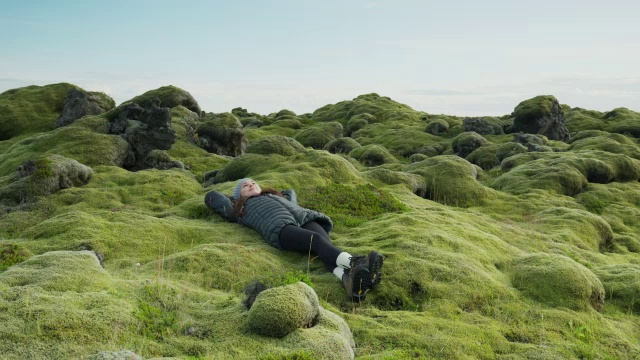 宽摇摄女人躺在长满苔藓的风景/冰岛视频素材