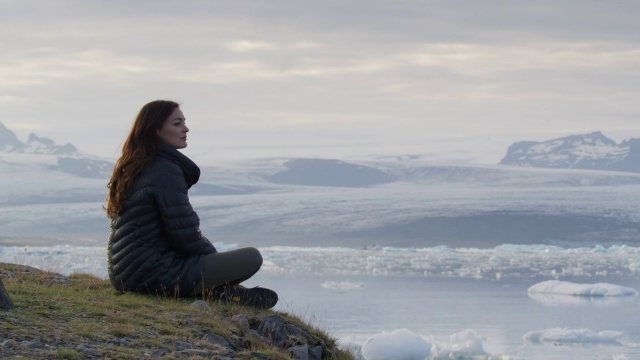 中等镜头的女人坐在山上欣赏冰川泻湖/ Jokulsarlon，冰岛视频素材