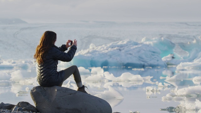 中镜头的女人坐在岩石上拍摄冰川泻湖/ Jokulsarlon，冰岛视频素材