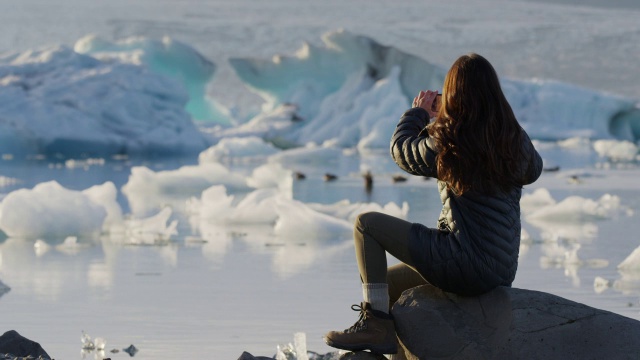 妇女在冰川泻湖拍摄鸭子的中景/冰岛Jokulsarlon视频素材