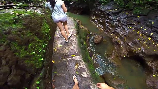 在巴厘岛旅游度假期间，一对旅行者在一条狭窄的河流裂缝中行走，用动作摄像机从个人角度记录下来。视频素材