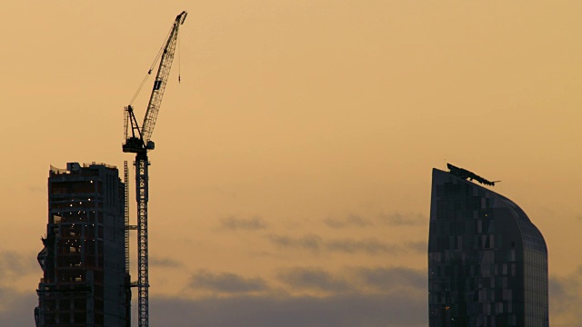 大型建筑起重机耸立在摩天大楼上，映衬着纽约市橙色的天空。视频素材