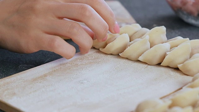 女人用碎肉包饺子，特写的手。把饺子放在木板上。视频素材