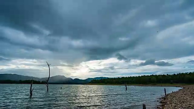 日落在岩石海滩和湖与树桩和热带山脉背景视频素材