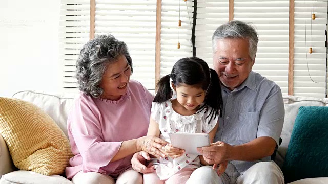 小女孩过来拥抱正在玩平板电脑的一男一女。孩子和年长的男人和女人玩，带着快乐的情绪。人有家庭、生活方式、科技理念。4 k的决议视频素材