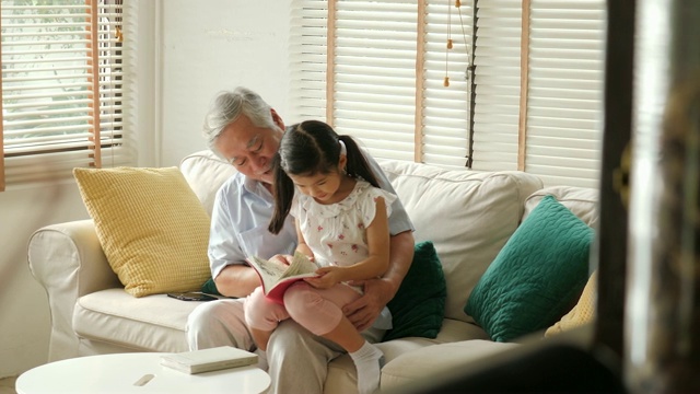 亚洲老爷爷和小孙女一起在家看书。高级生活方式家庭理念。视频素材