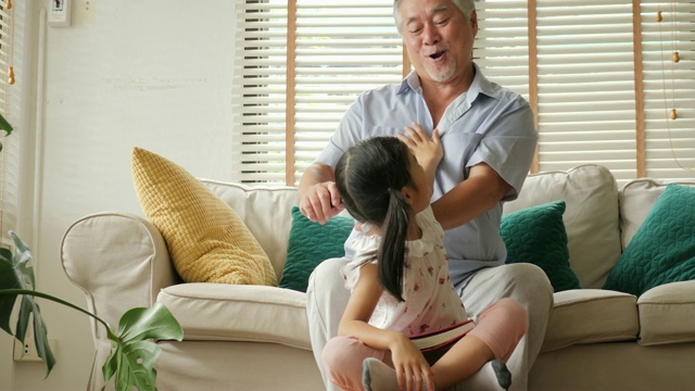 亚洲老爷爷在小女孩在家看书时扎她的头发。人有家庭、生活方式、教育理念。视频素材