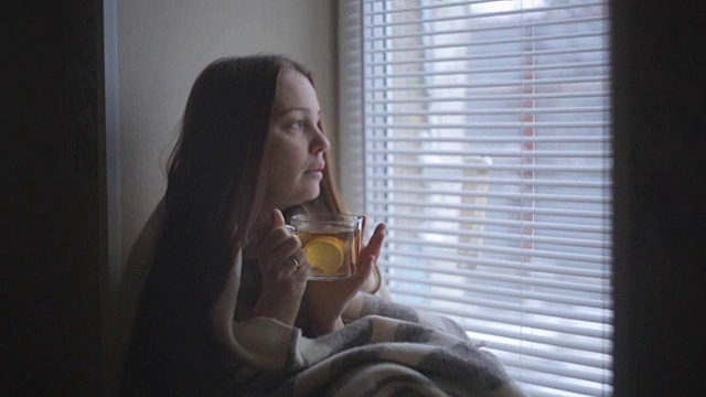 一个生病的漂亮女人感冒了，喝着柠檬热茶，坐在一个乡村房子的窗户在冬天视频素材画面2