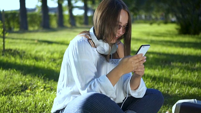 小女孩在外面的公园里微笑着用智能手机发短信视频素材