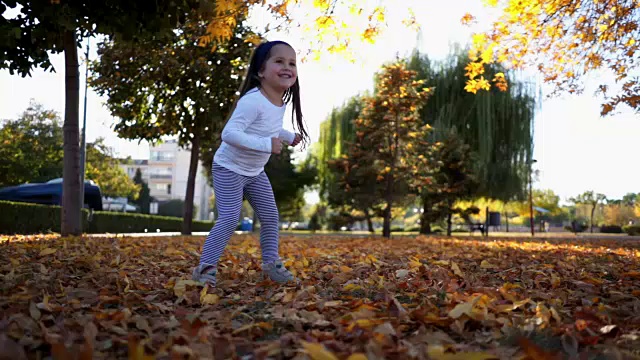 可爱的幼童在秋天公园的落叶中跳舞视频素材