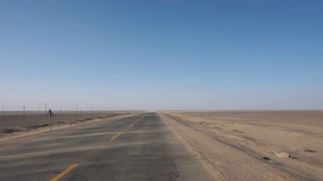 有人开着车在空旷的沙漠道路上行驶，沙子随风在路上移动，看起来像海浪，司机的看法。视频素材