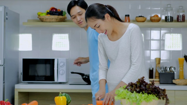 烹饪健康的食物。幸福的年轻夫妇一起在厨房做饭，而男人触摸他怀孕的妻子的腹部。怀孕和生育视频素材