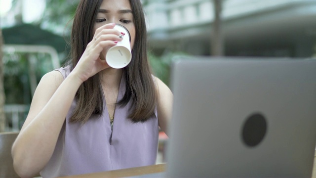 年轻女子喝着咖啡，在户外咖啡馆用笔记本电脑工作。视频下载