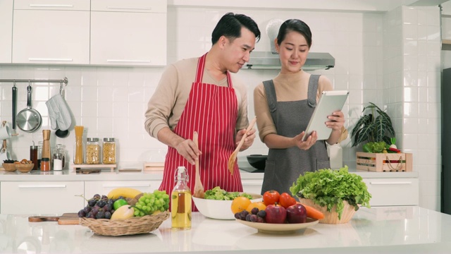 正面:日本妻子帮助丈夫烹饪食物，建议如何制作数字平板电脑视频素材