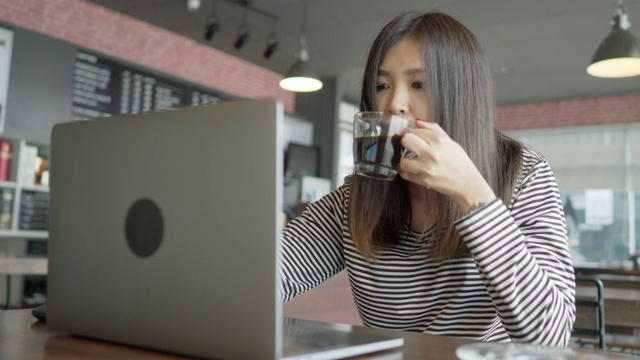 美丽的亚洲年轻女子工作在笔记本电脑和喝咖啡在咖啡馆视频下载