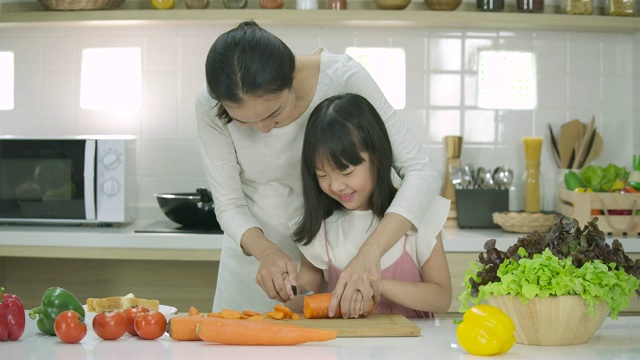 微笑着的怀孕母亲和女儿喜欢在厨房里一起准备健康的晚餐。母亲教女儿做饭。视频素材