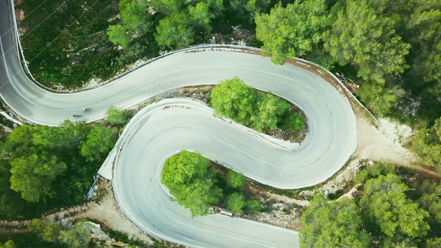 鸟瞰图的视频，两个骑自行车的人在森林里的一条双车道弯曲的道路视频素材