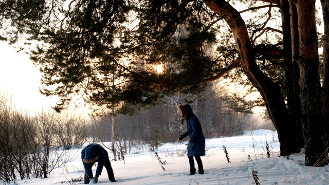 男人和女人在冬天的森林里玩雪球。冬日森林里的日落视频素材