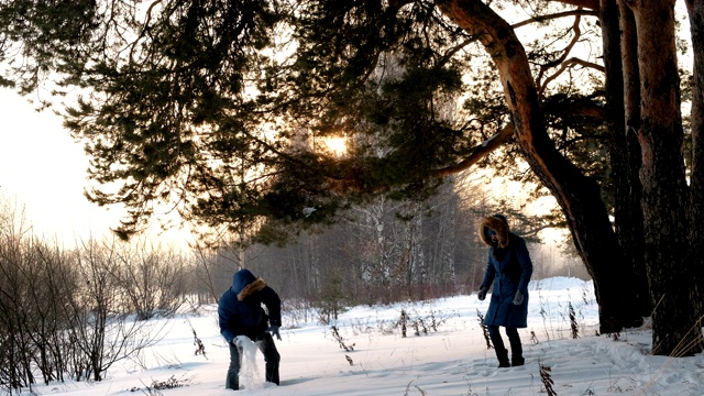 男人和女人在冬天的森林里玩雪球。冬日森林里的日落视频素材