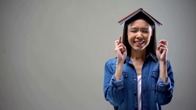 年轻女子站在交叉手指和书在她的头上，学生仪式视频素材