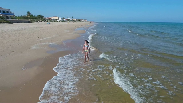 那个女孩在沙滩上沿着海岸跑。视频素材