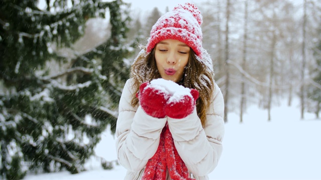 快乐的年轻女子吹雪在冬天的森林视频素材