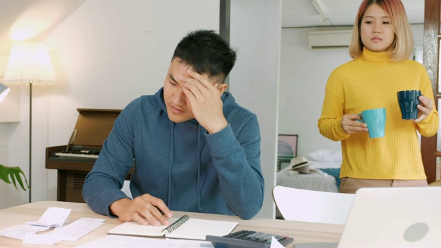 亚洲女性女友鼓励男友从压力，而工作在家里的客厅笔记本电脑上的家庭预算视频素材