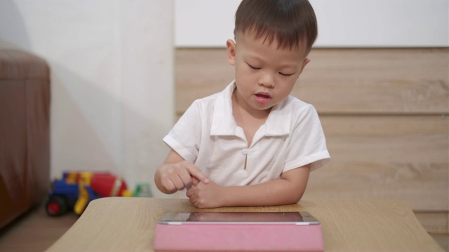 可爱的小微笑亚洲2 - 3岁的蹒跚学步的婴儿男孩坐在地板上看一个视频从平板电脑。孩子们在玩平板电脑视频素材