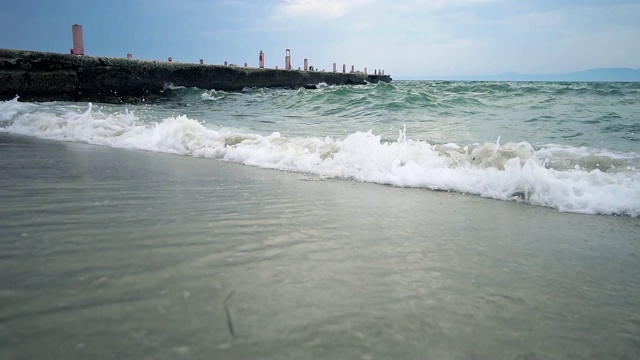 自然背景，海浪溅起沙滩上的沙子，以码头为背景，慢镜头视频素材