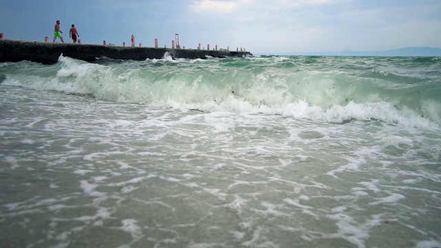 自然背景，海浪溅起沙滩上的沙子，以码头为背景，慢镜头视频素材