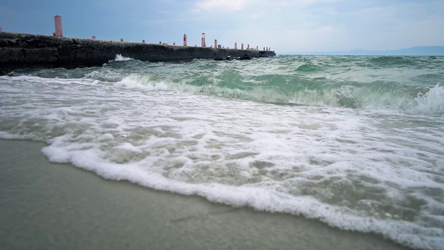 自然背景，海浪溅起沙滩上的沙子，以码头为背景，慢镜头视频素材